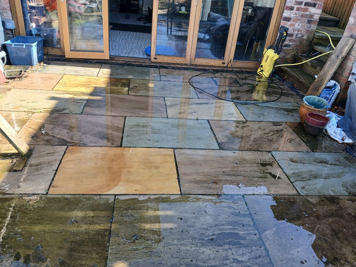 Partially cleaned sandstone patio during pressure washing, showing the contrast between dirty and clean paving slabs.