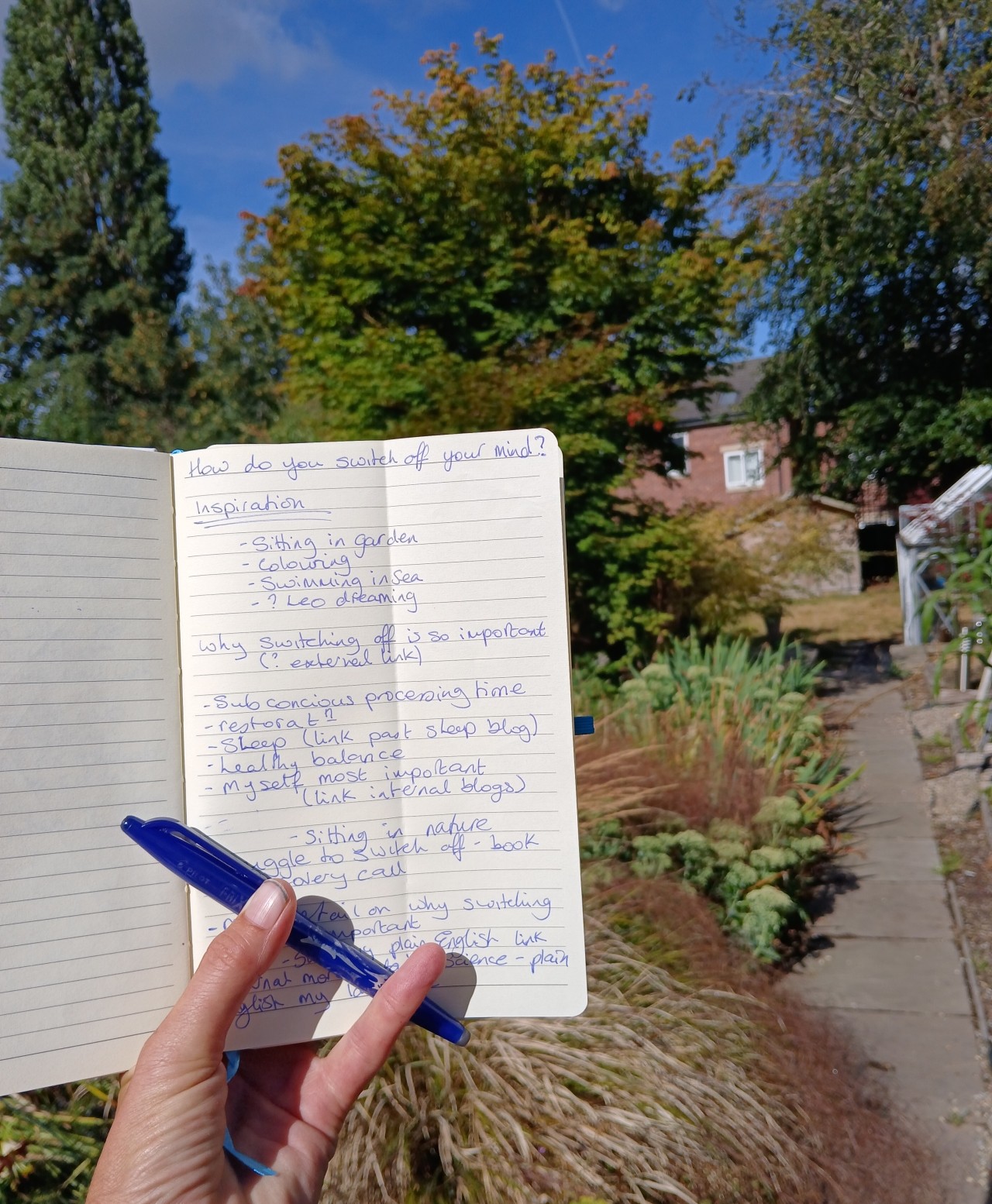 Open notebook and pen held in a sunny garden beneath a blue sky, capturing ideas and inspiration for small business blogs.